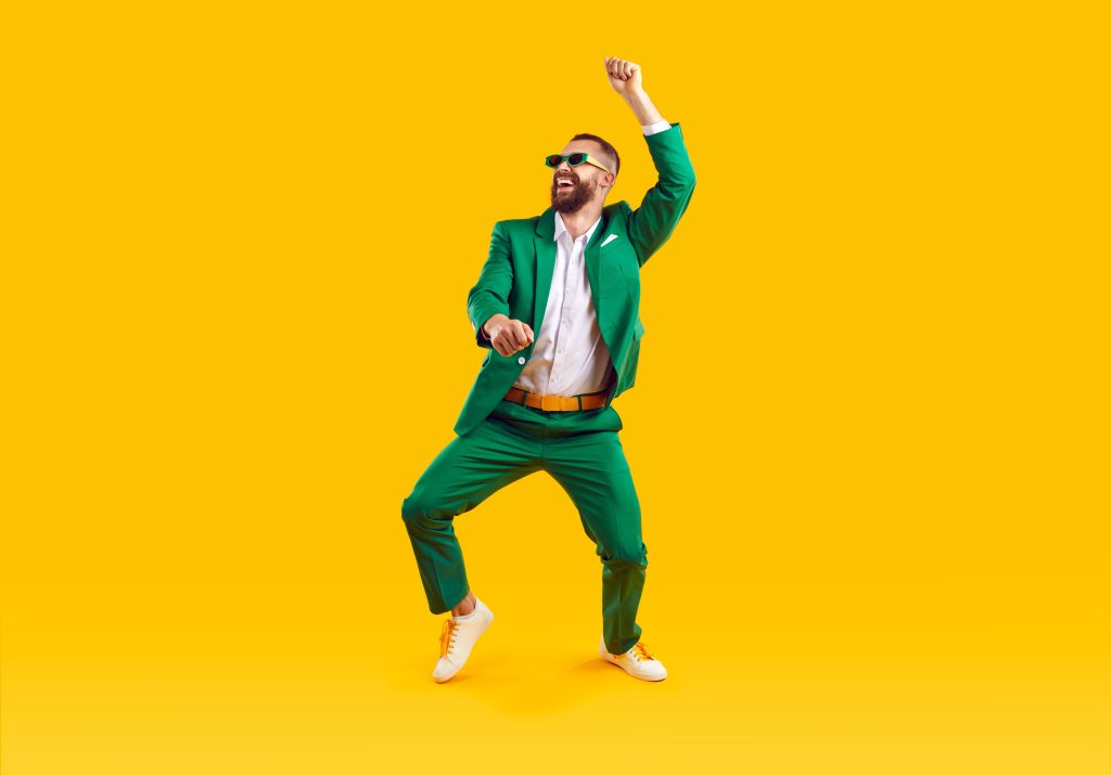 Bărbat cu ochelari de soare și îmbrăcat în costum verde care dansează Gangnam Style pe un fundal galben.