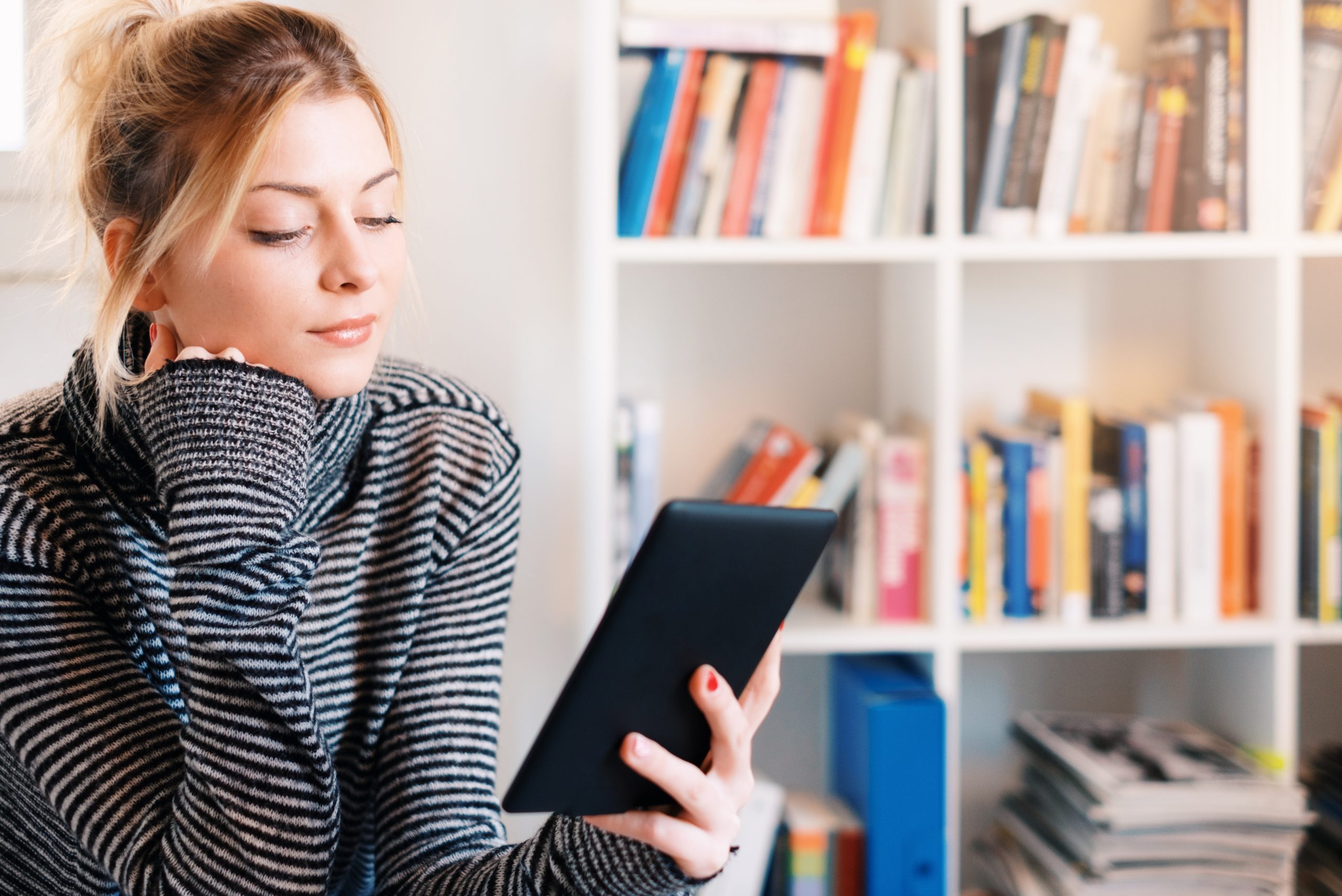 Fată care citește pe Kindle o carte de pe BookTok în bibliotecă.