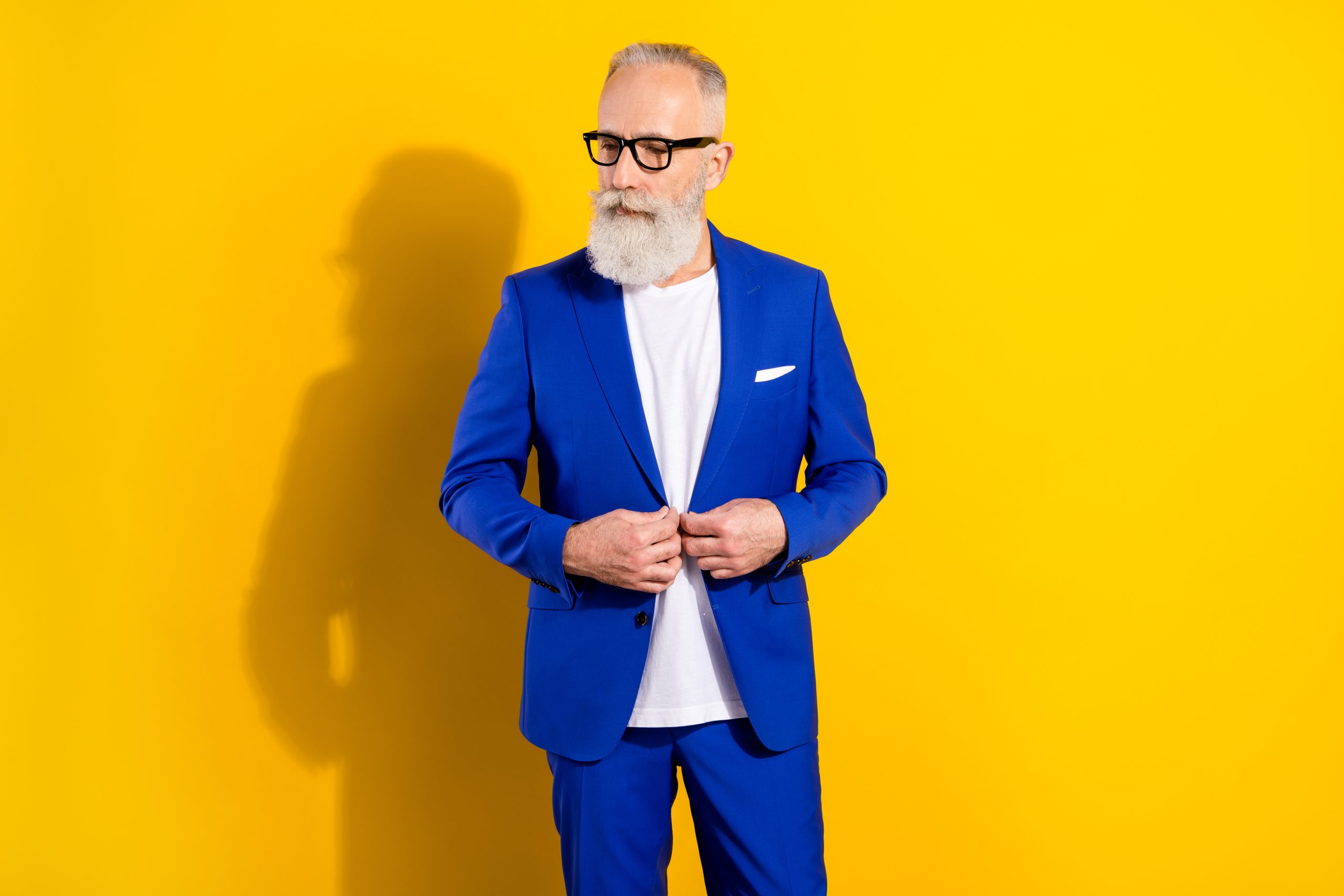 Bărbat ce poate fi un director de creație, îmbrăcat în costum albastru, cu barbă și ochelari, pe fundal galben.