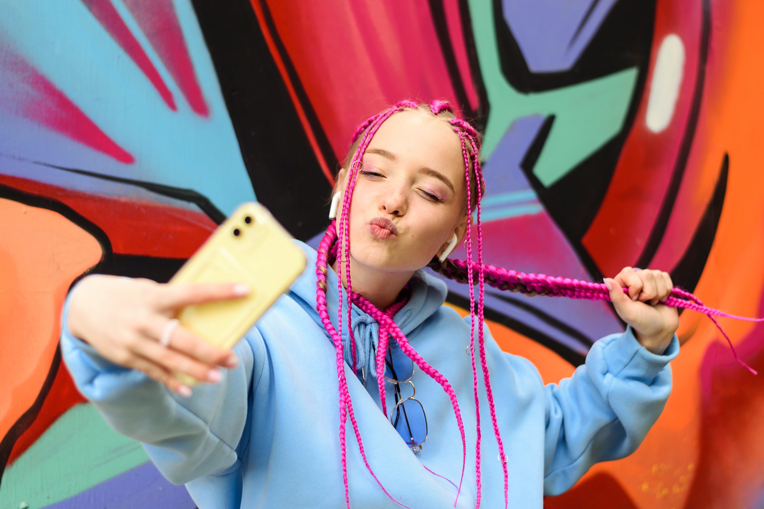 Fată Gen Alpha cu codițe împletite roz își face un TikTok cu un smartphone galben pe un perete colorat.